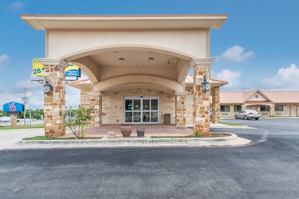 A hotel entrance with a stone facade, a covered patio, and a clear sky.