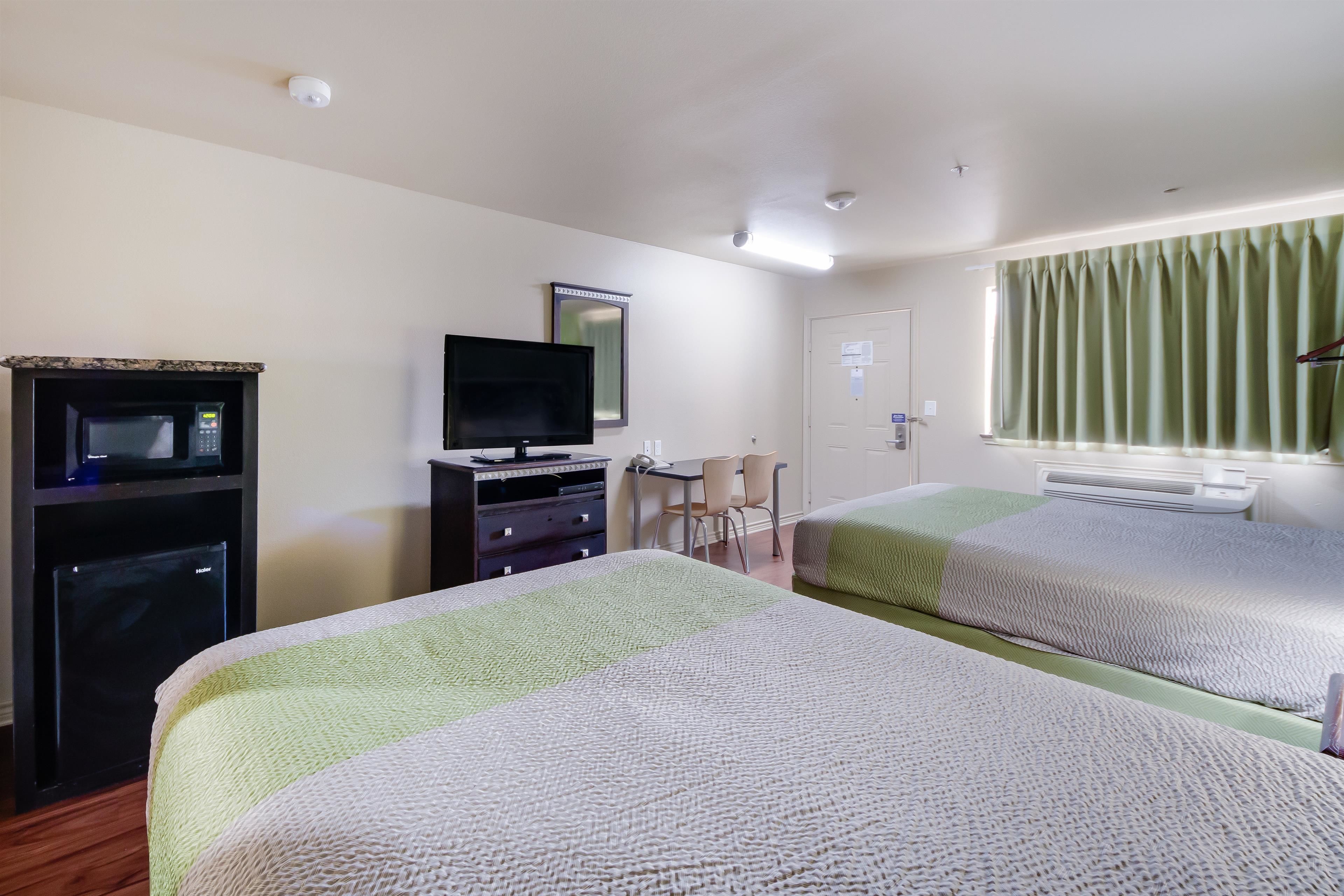 A hotel room with two beds, a desk with a chair, a television, and a microwave.