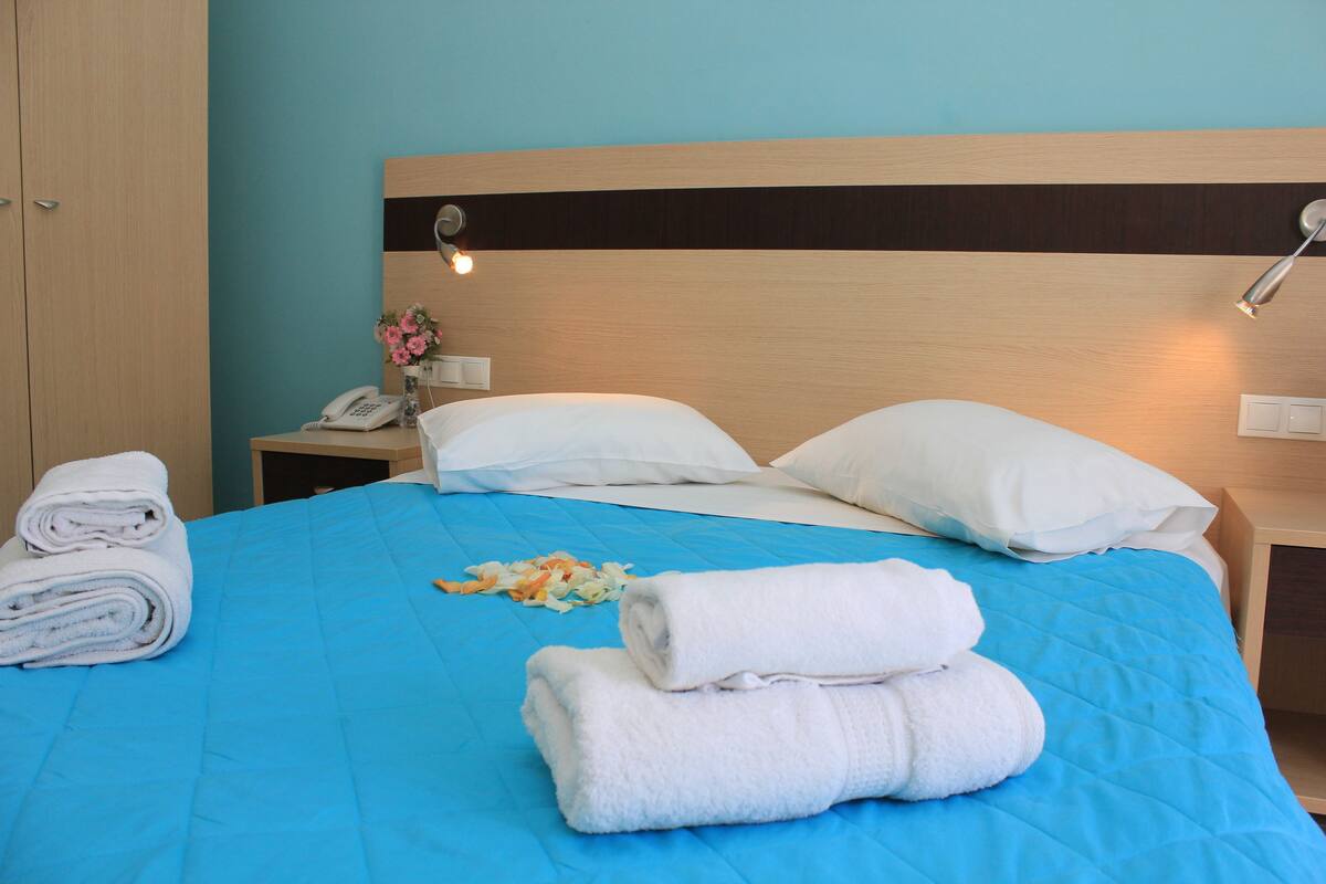 A neatly made bed with blue bedding, white pillows, and rolled towels.