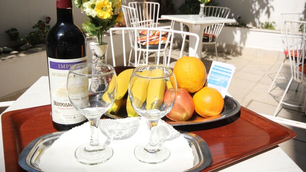 Un plateau avec une bouteille de vin de Maïkop, deux verres à vin et une assiette de fruits, notamment des bananes, des pommes et des oranges.