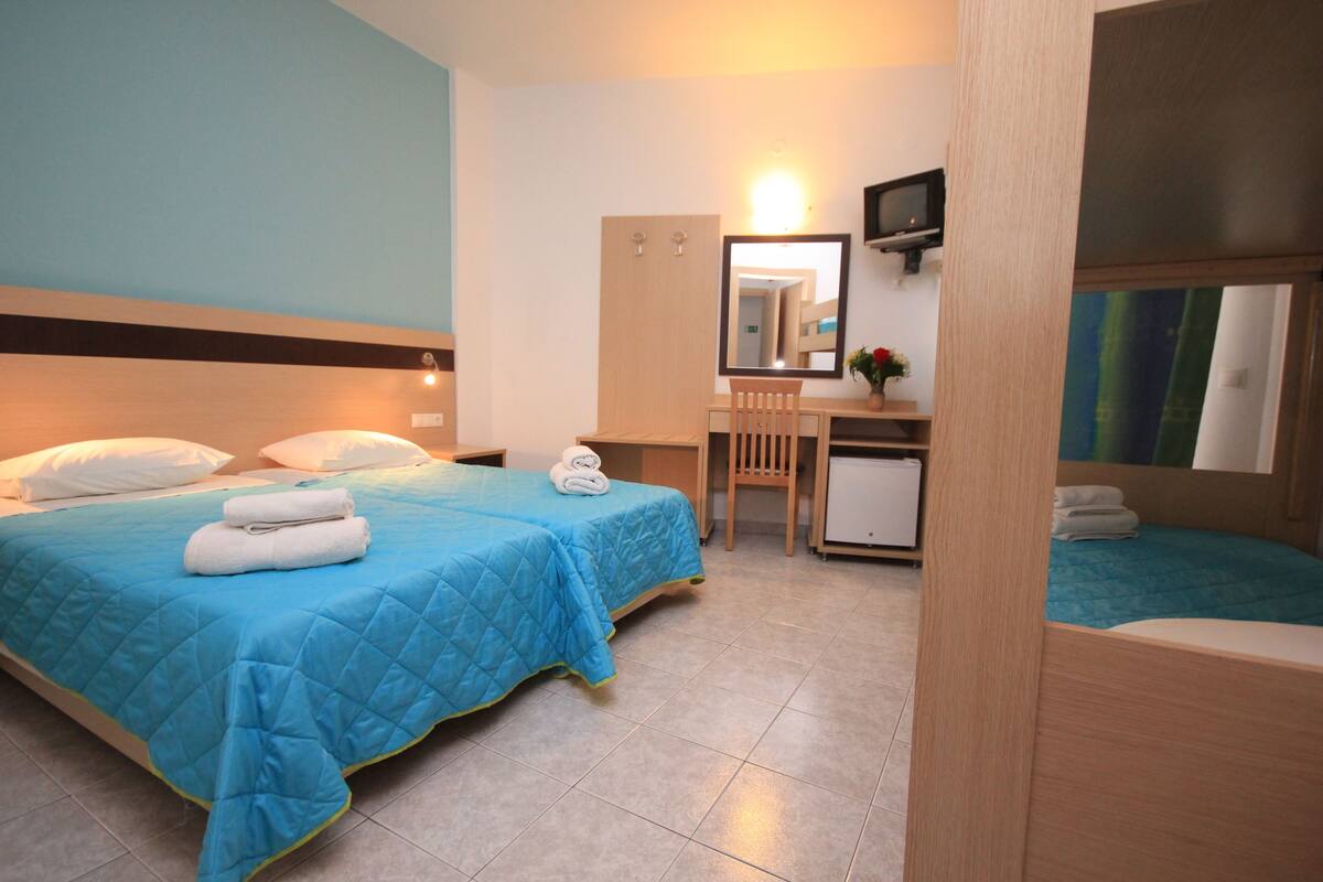 A hotel room with a bed, a desk, a chair, a small TV, and a mirror.