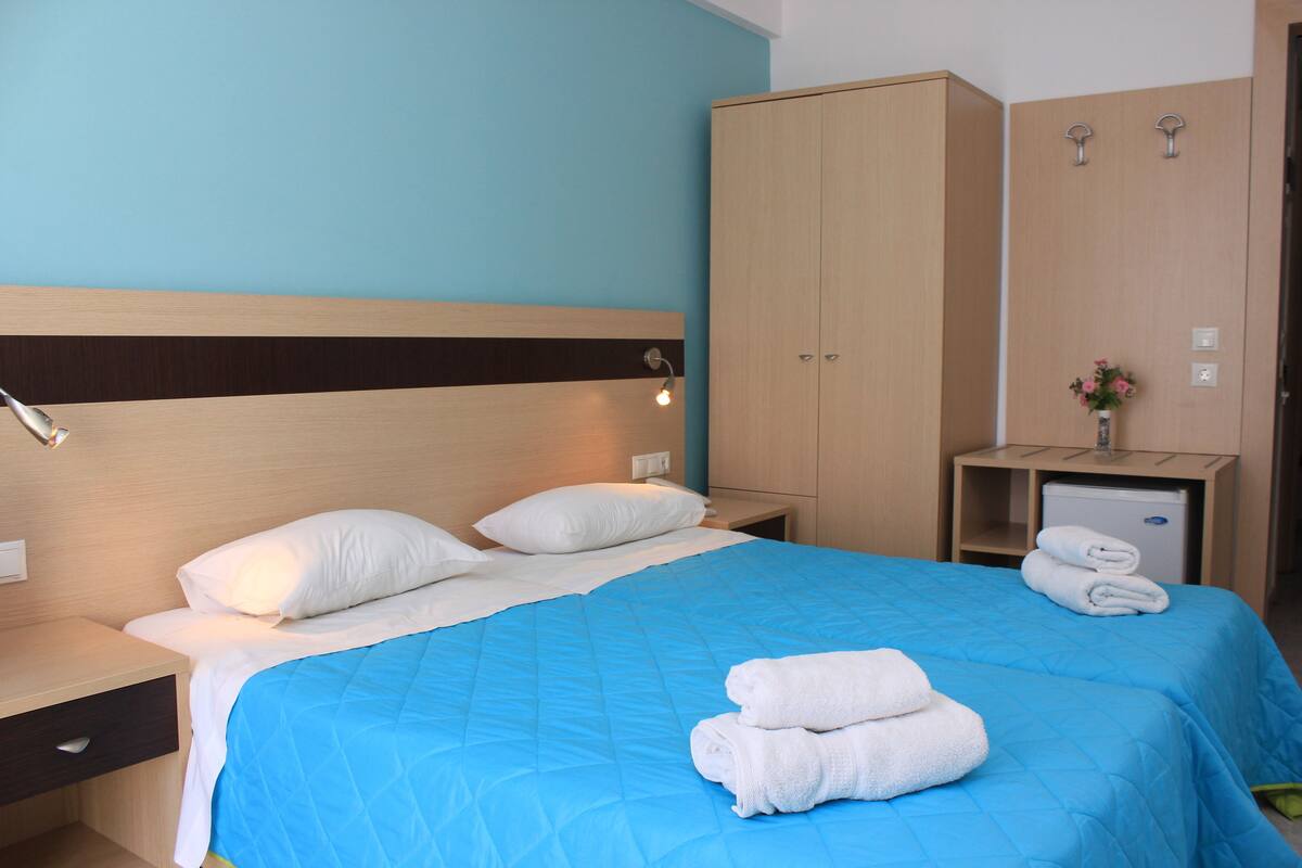A hotel room with a bed, a nightstand, a wardrobe, and a small desk with a lamp.