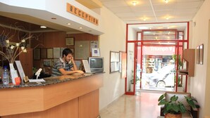 Un comptoir d’accueil avec un homme derrière, un téléviseur et une pancarte indiquant « RÉCEPTION ».