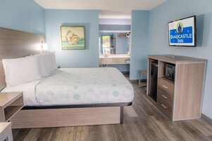 A hotel room with a bed, a desk, a television, and a bathroom visible through an open door.