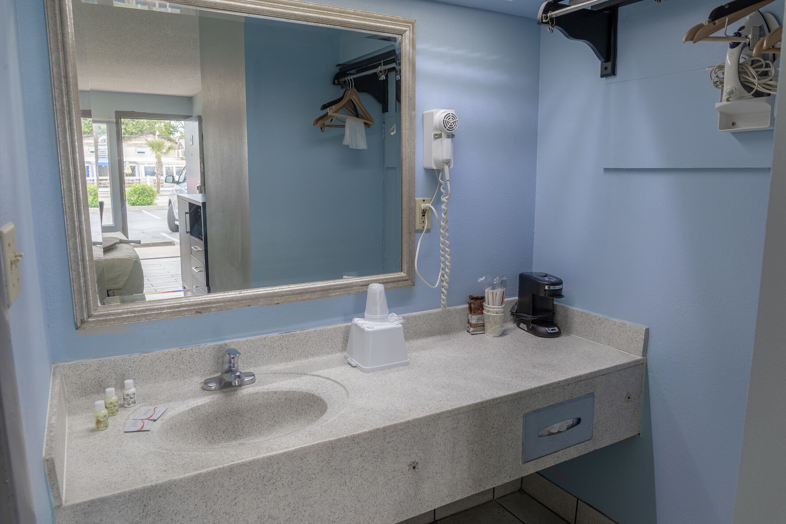 A bathroom with a sink, mirror, hair dryer, and a coffee maker.