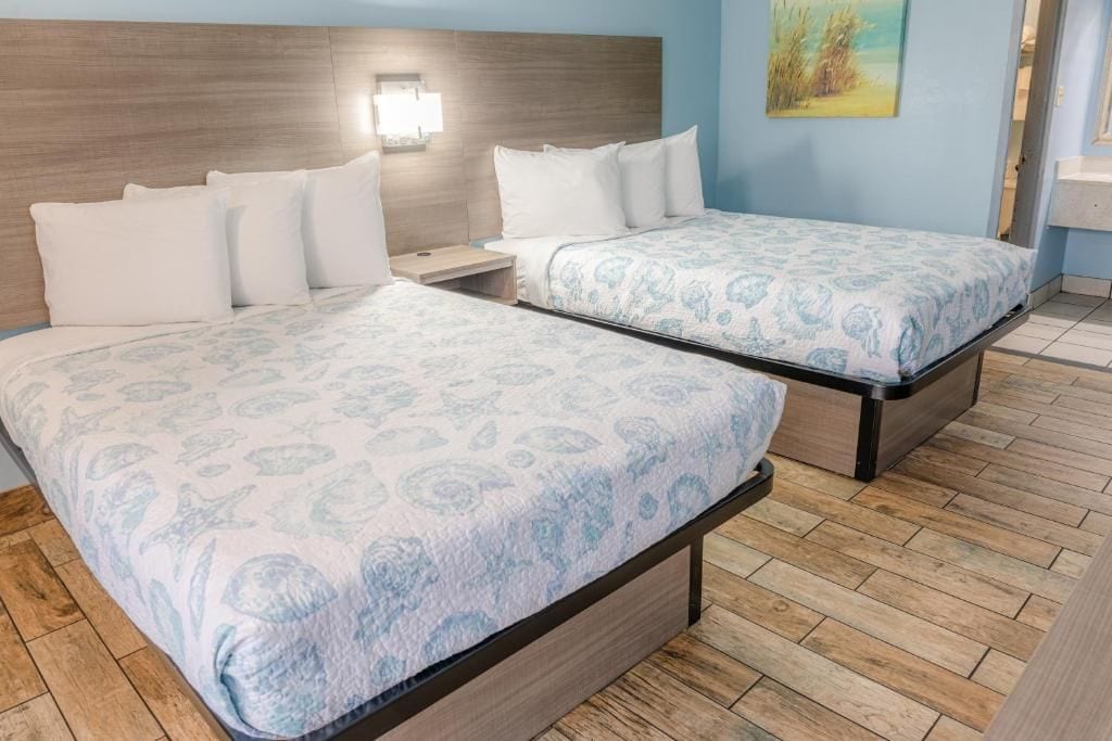 A hotel room with two beds, wooden headboard, a nightstand, and a painting on the wall.