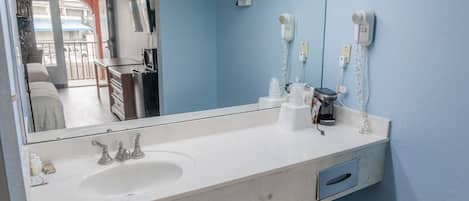 A bathroom with a white sink, a mirror, a hairdryer, and a towel rack.