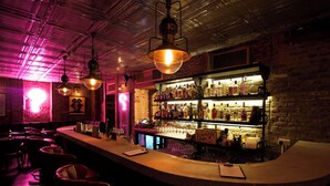 A bar area with a curved counter, hanging pendant lights, and a brick wall backdrop. - Artist Residence London (London)