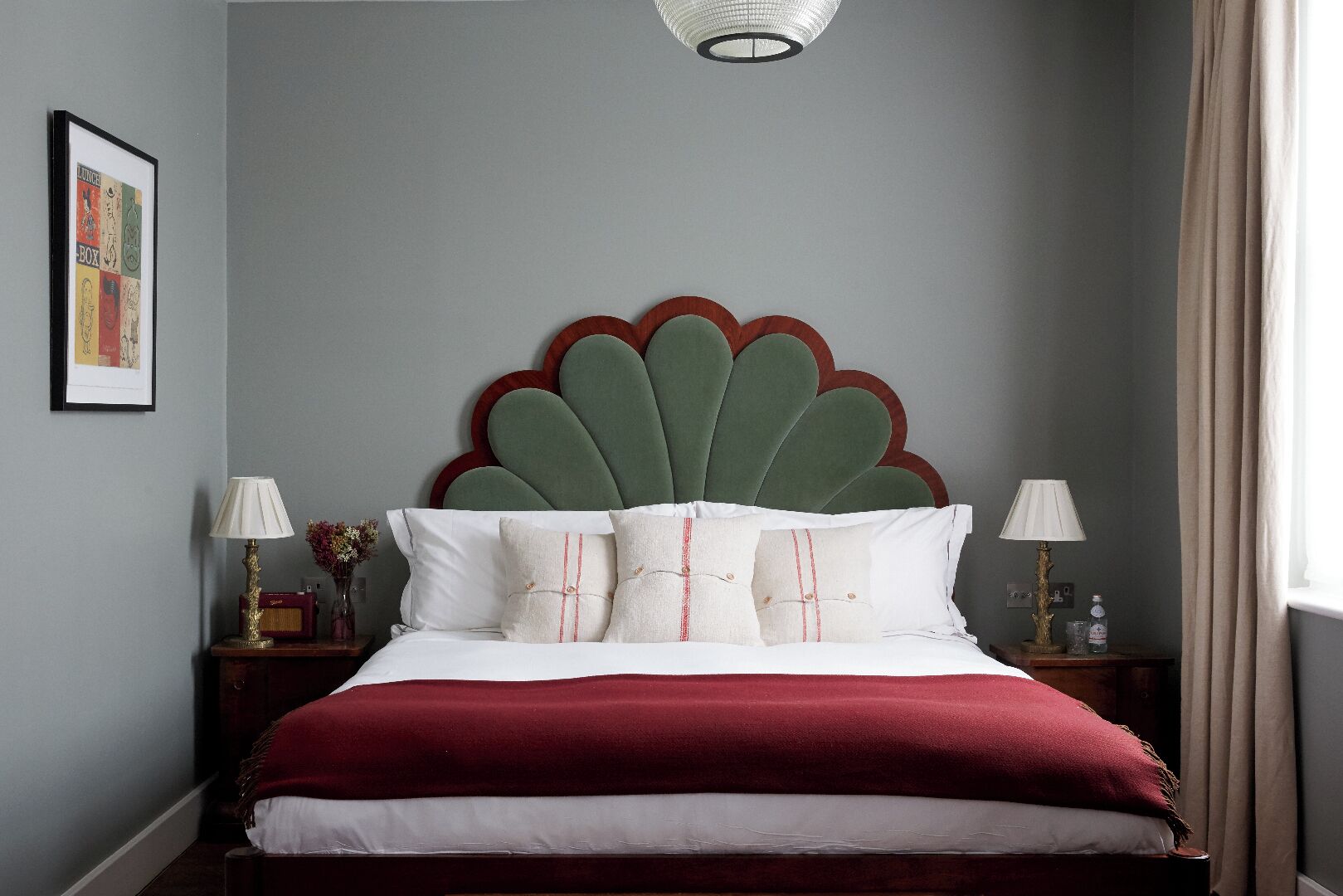 A bedroom with a bed, two bedside tables, a wall-mounted lamp, and a framed picture.