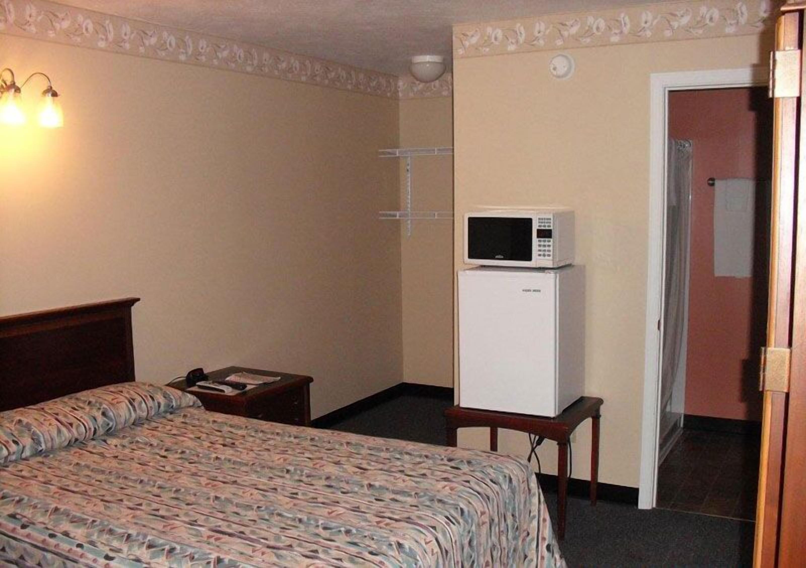 A hotel room with a bed, a bedside table, a microwave, and a door leading to another room.