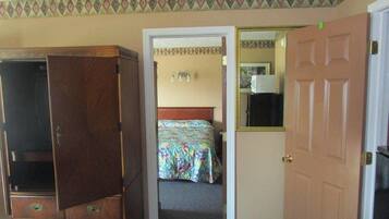 A room with a wooden wardrobe, a bed with a floral bedspread, and a door leading to another room.