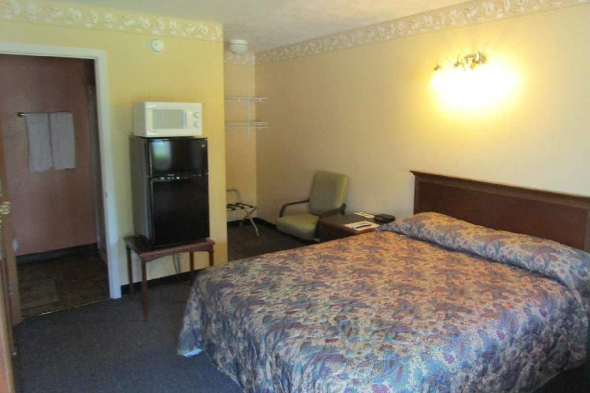 A hotel room with a bed, a microwave, a chair, and a desk.
