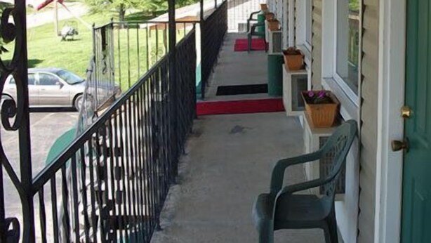 A covered porch with a metal railing, a red carpet, and a green chair.