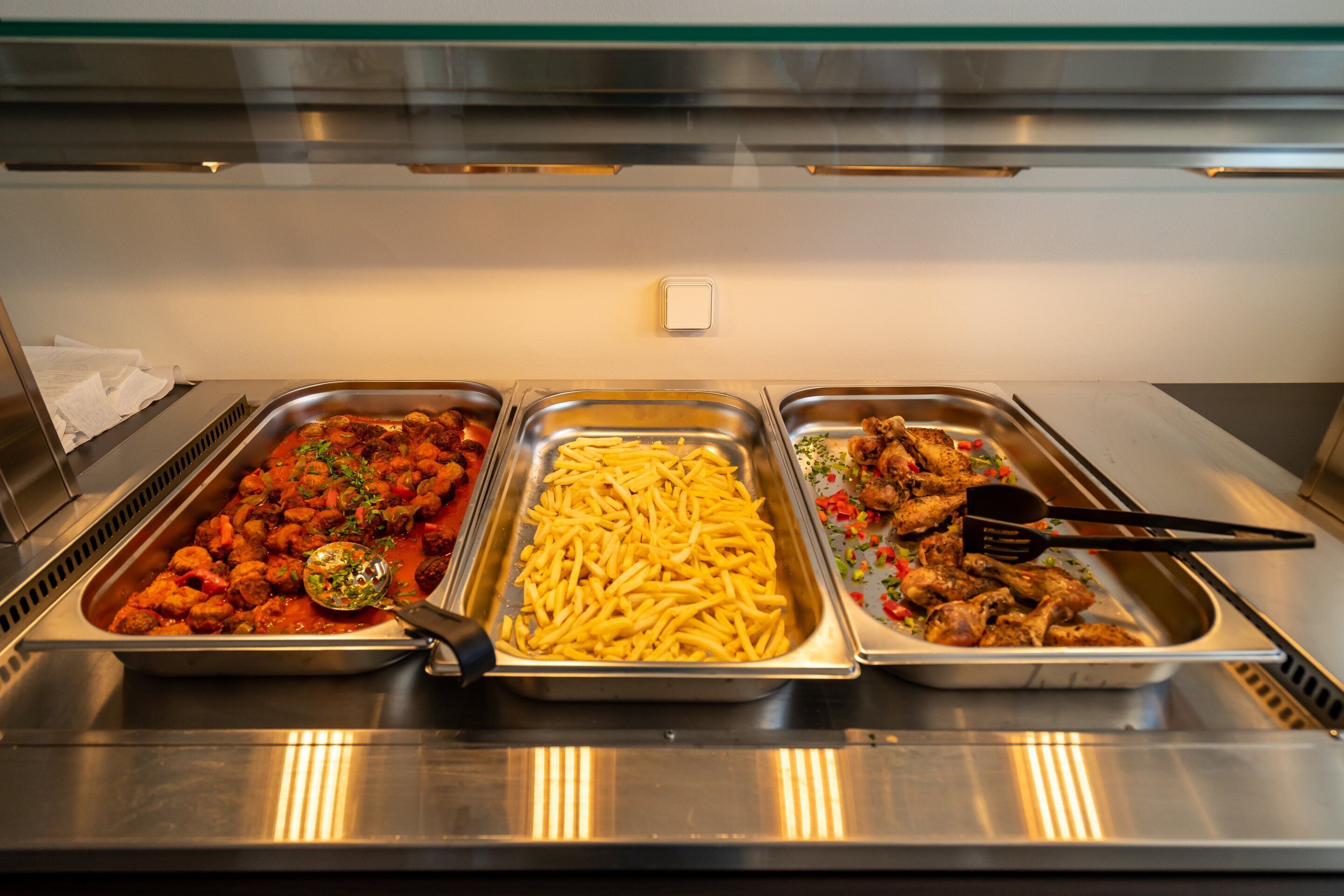 Een buffet met drie schalen eten: gehaktballetjes in tomatensaus, friet en kip met groenten.
