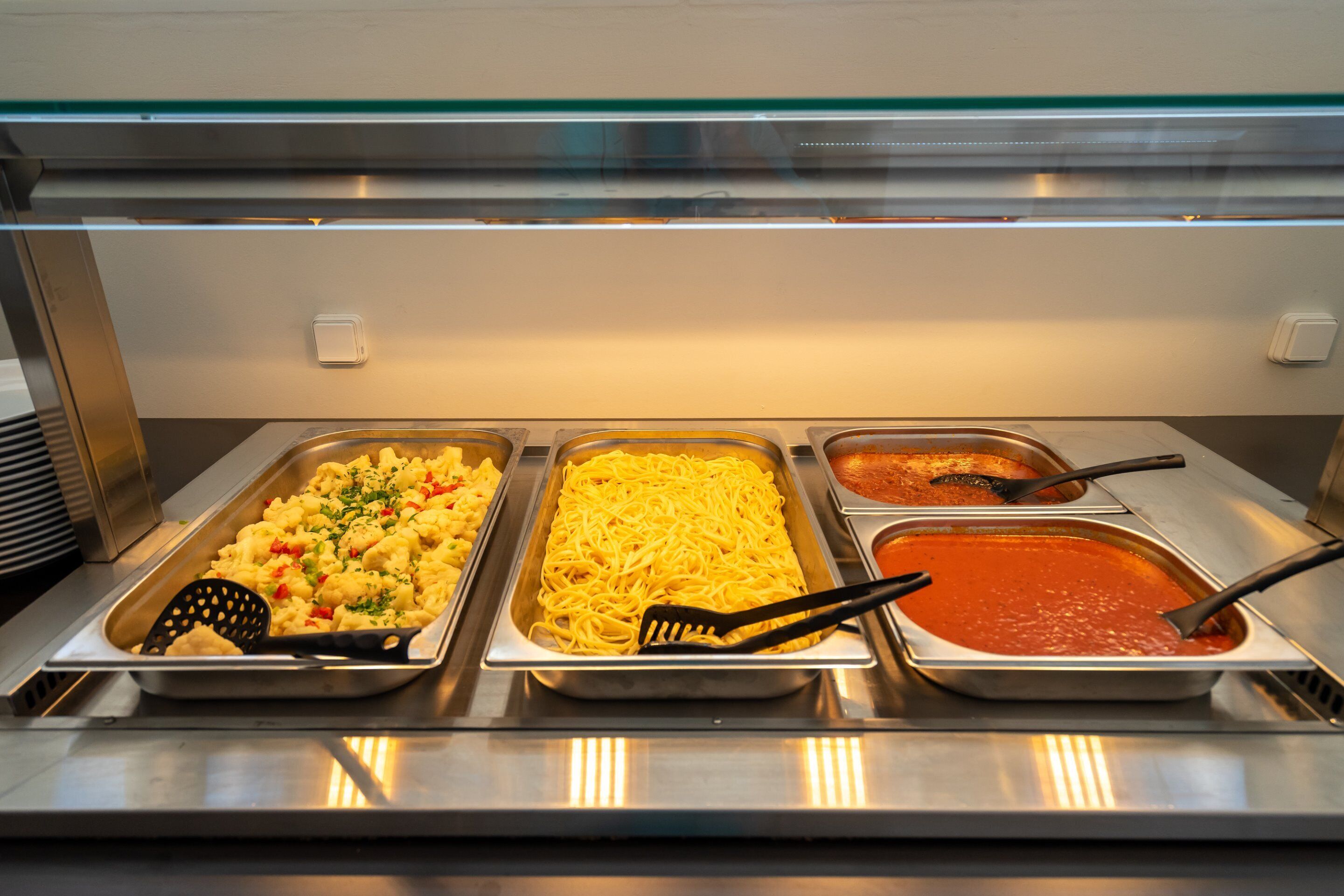 A buffet with pasta, a pasta salad, and a tomato-based dish.