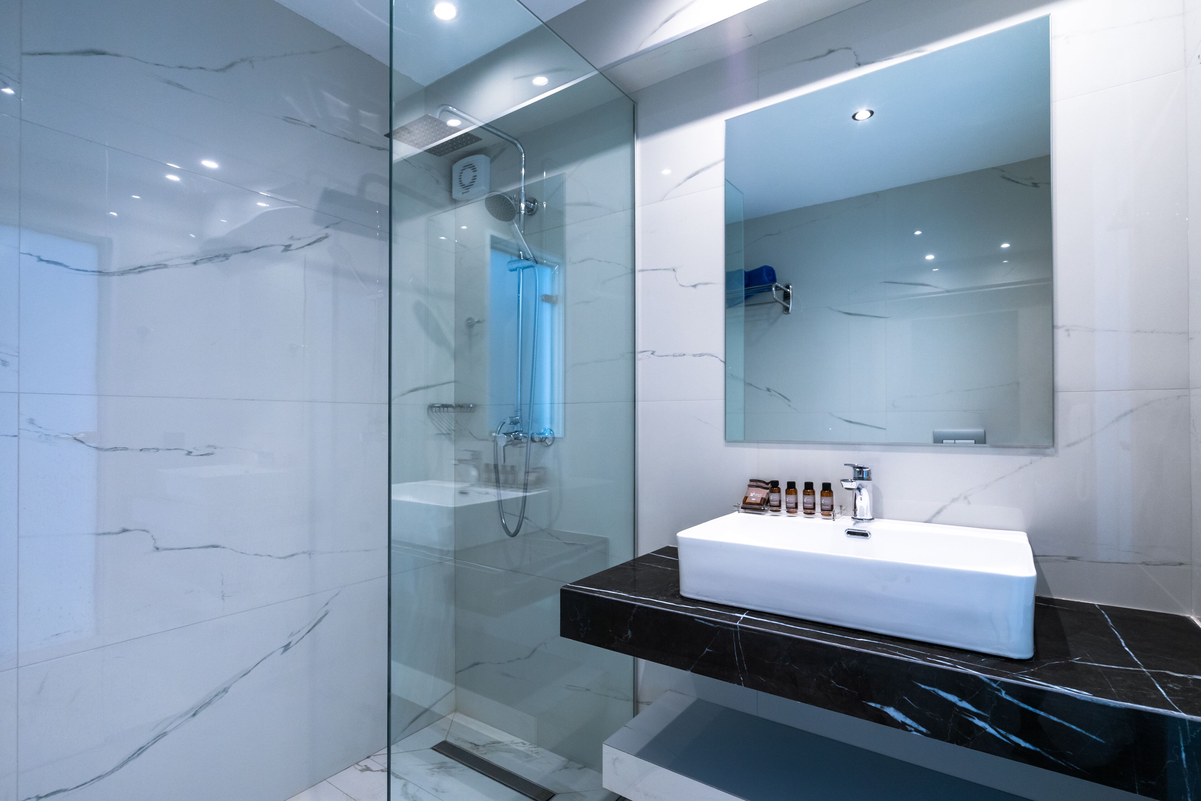 A modern bathroom with a glass-enclosed shower, a white sink, and a large mirror.