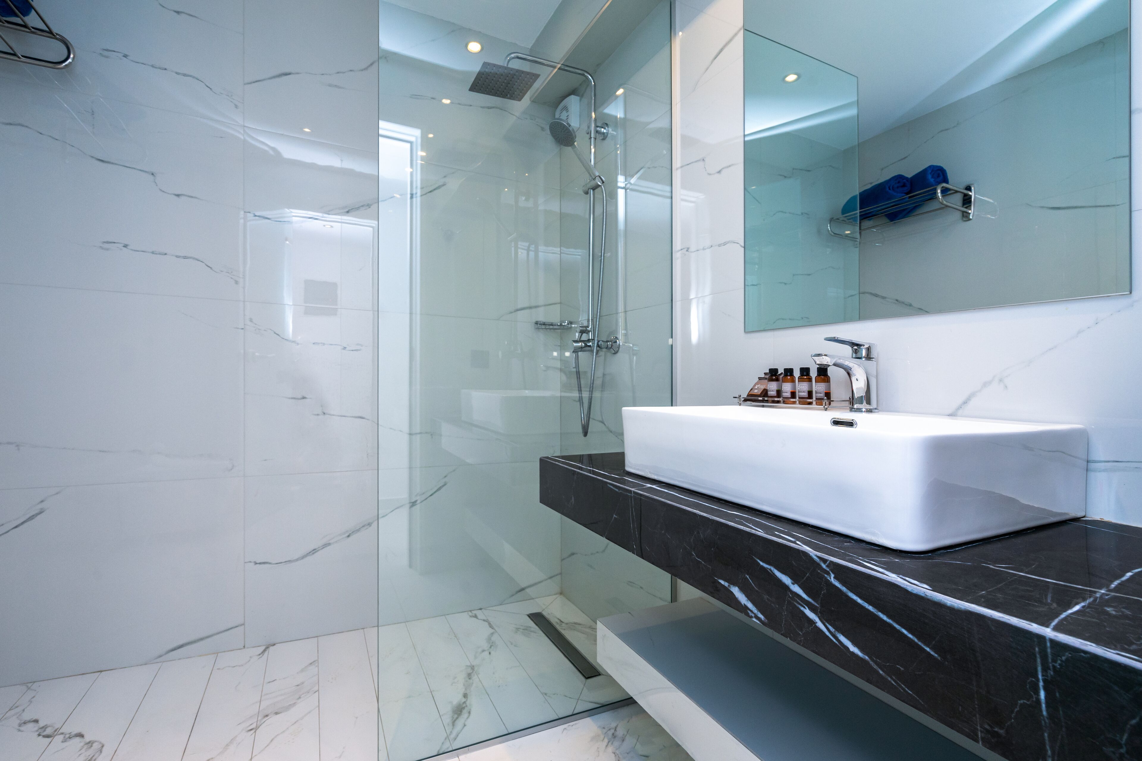 Un baño moderno con ducha envuelta en vidrio, un lavabo blanco y suelo de mármol.