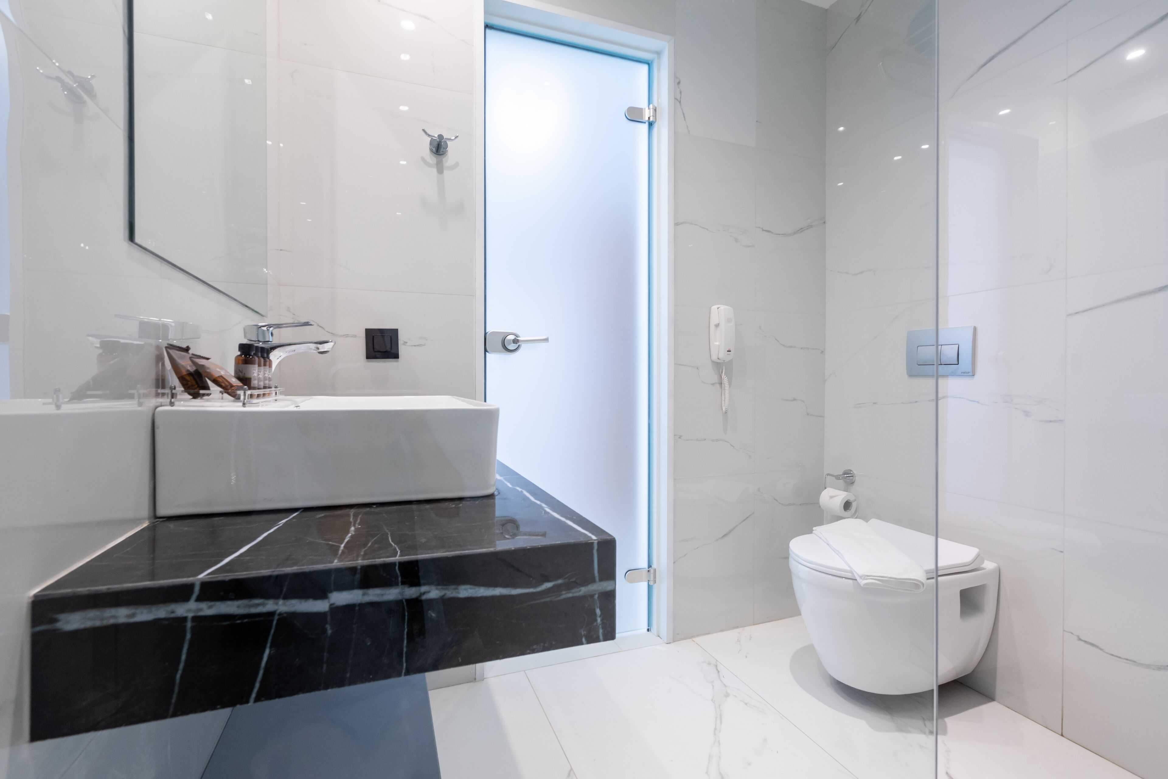 A modern bathroom with a black marble countertop, a white toilet, and a glass shower enclosure.