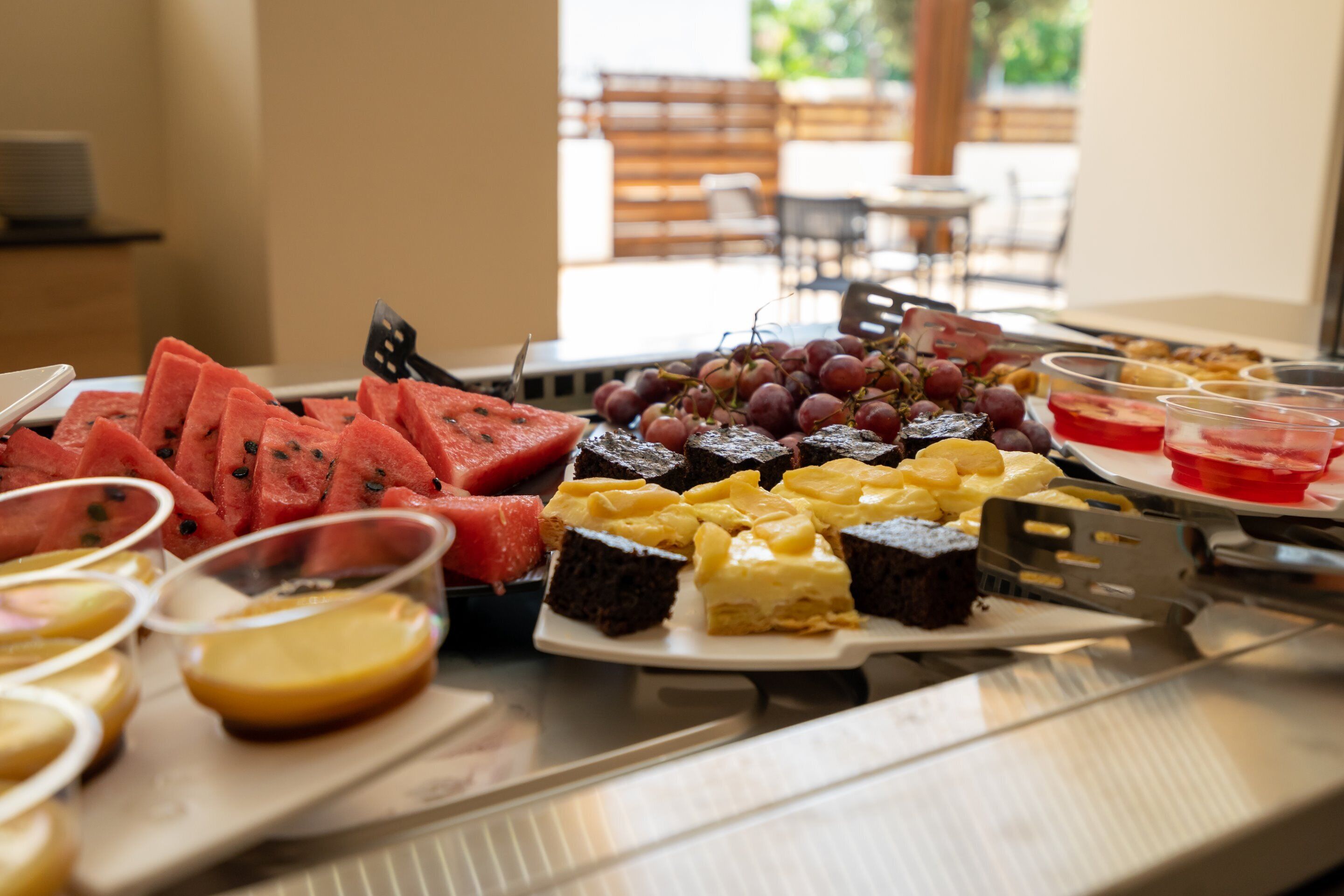A buffet table with various food items including watermelon, grapes, and desserts.