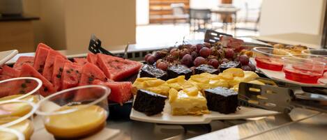 A buffet table with various food items including watermelon, grapes, and desserts.