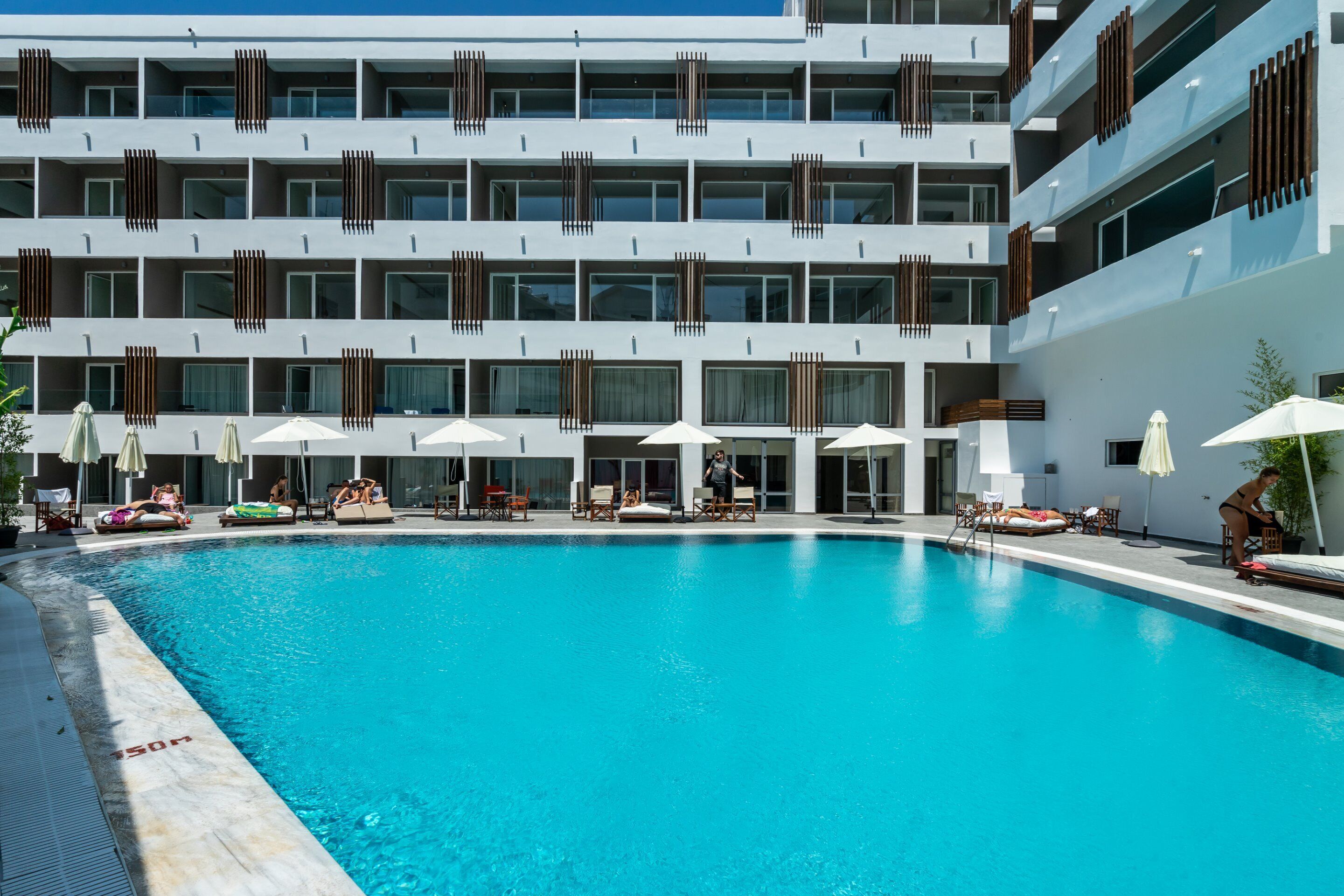 A modern hotel with a large pool, multiple balconies, and outdoor seating areas.