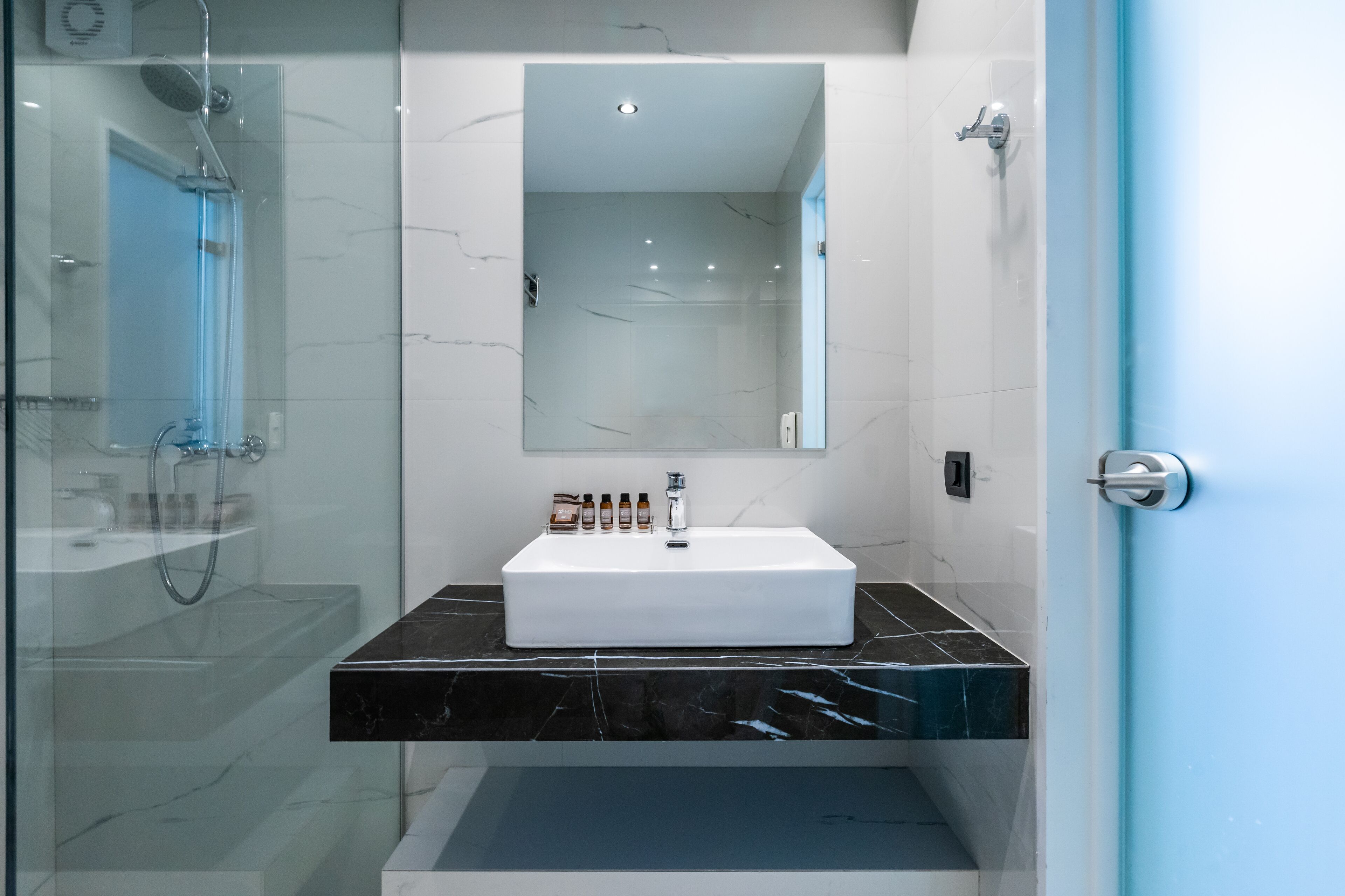 A modern bathroom with a glass-enclosed shower, a white sink with a marble countertop, and a large mirror above the sink.