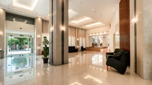 A spacious lobby with a glass entrance, a reception desk, and a seating area with a sofa and armchairs. - Castellum Suites (Rhodes)