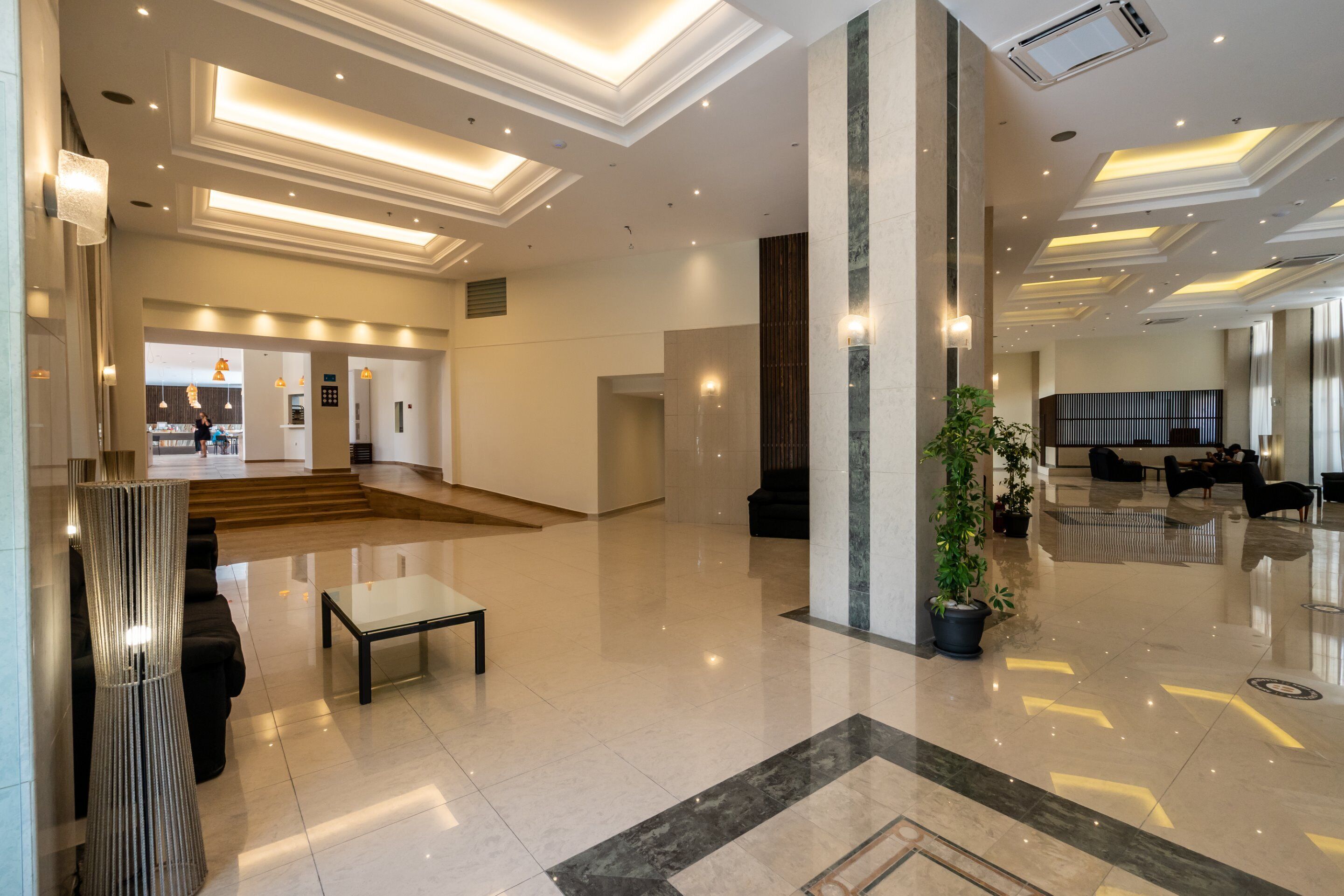 Um hall amplo com design moderno, apresentando uma escadaria central, uma área de estar com mesinha de café e um vaso de planta.