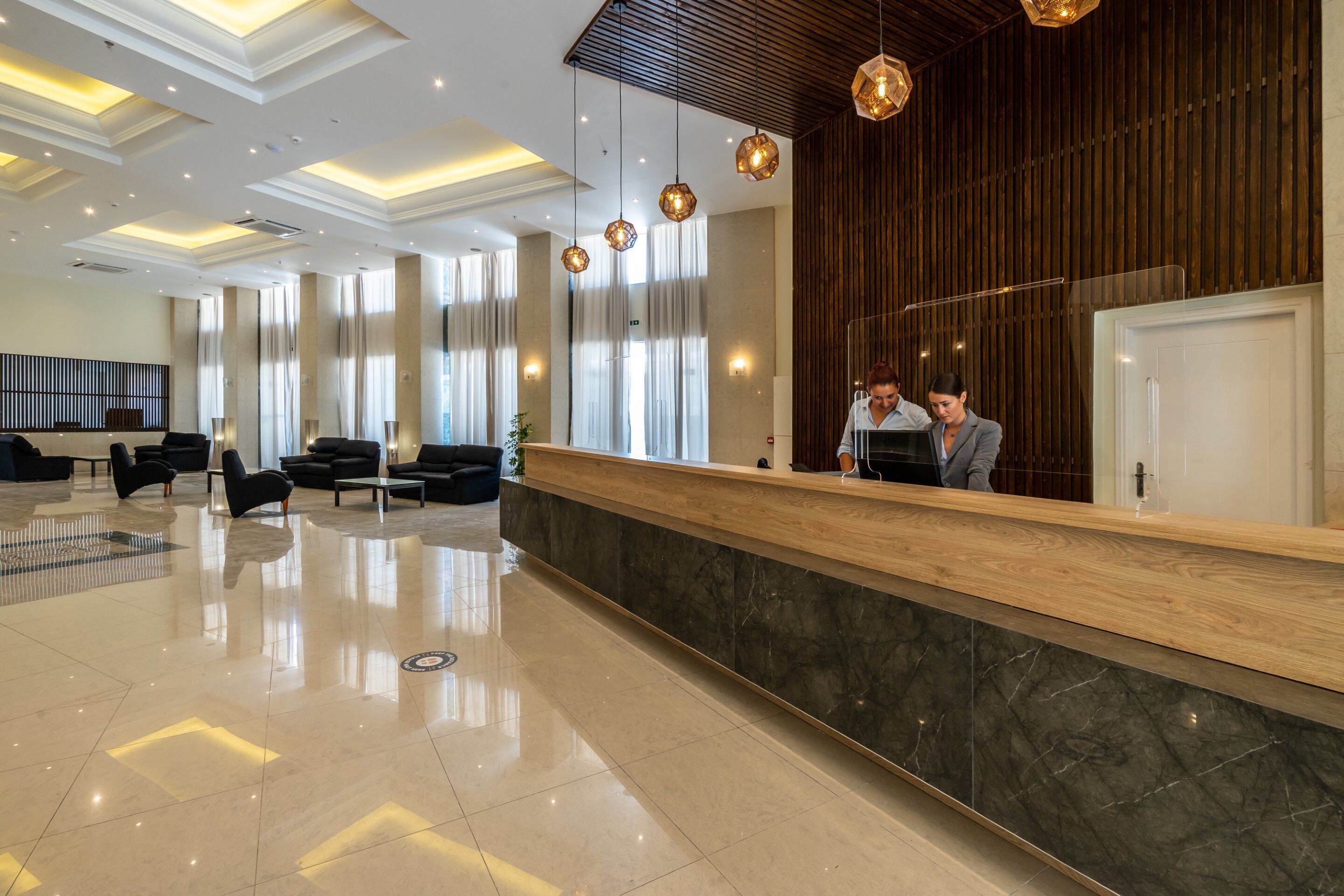 Een moderne hotellobby met een receptiebalie, zwarte lederen stoelen en een gepolijste marmeren vloer.