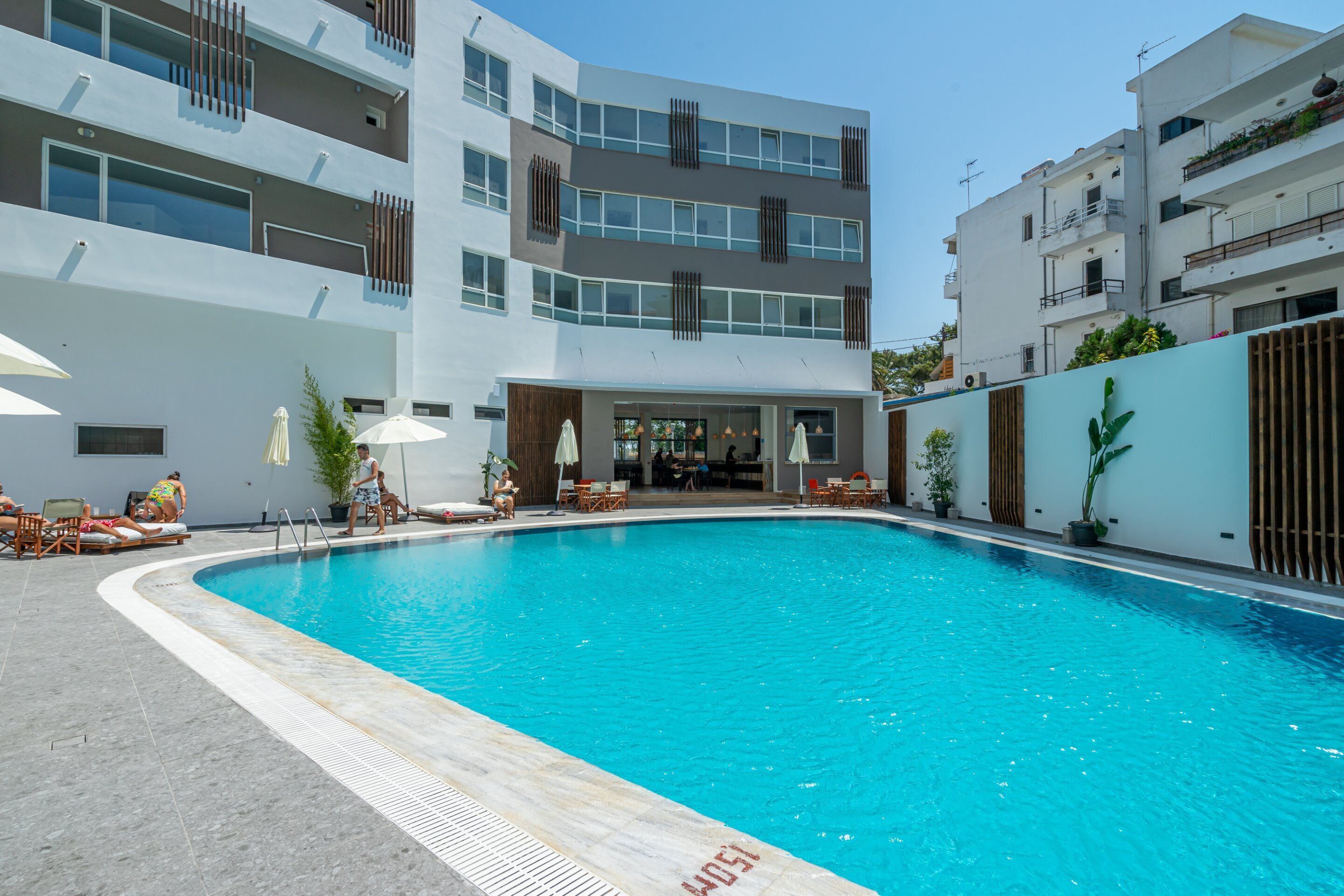A modern hotel with a swimming pool, outdoor seating, and a bar area.