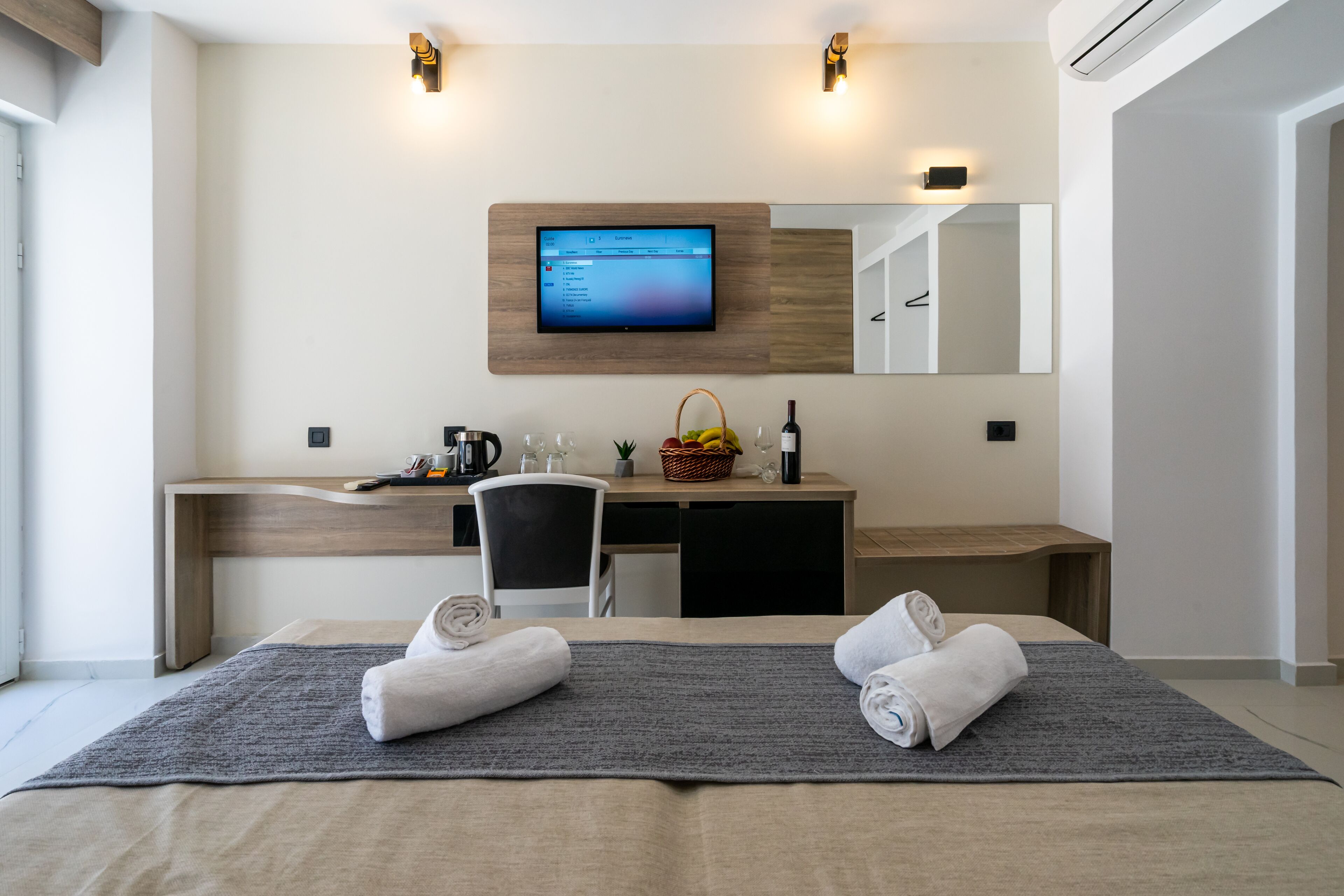 A modern hotel room with a large bed, a desk with a computer, a television mounted on the wall, and a small seating area.