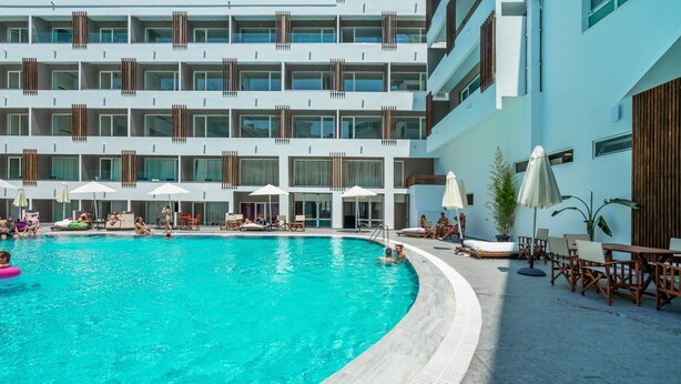 A swimming pool area with lounge chairs and umbrellas, surrounded by a multi-story building with balconies. - Castellum Suites (Rhodes)
