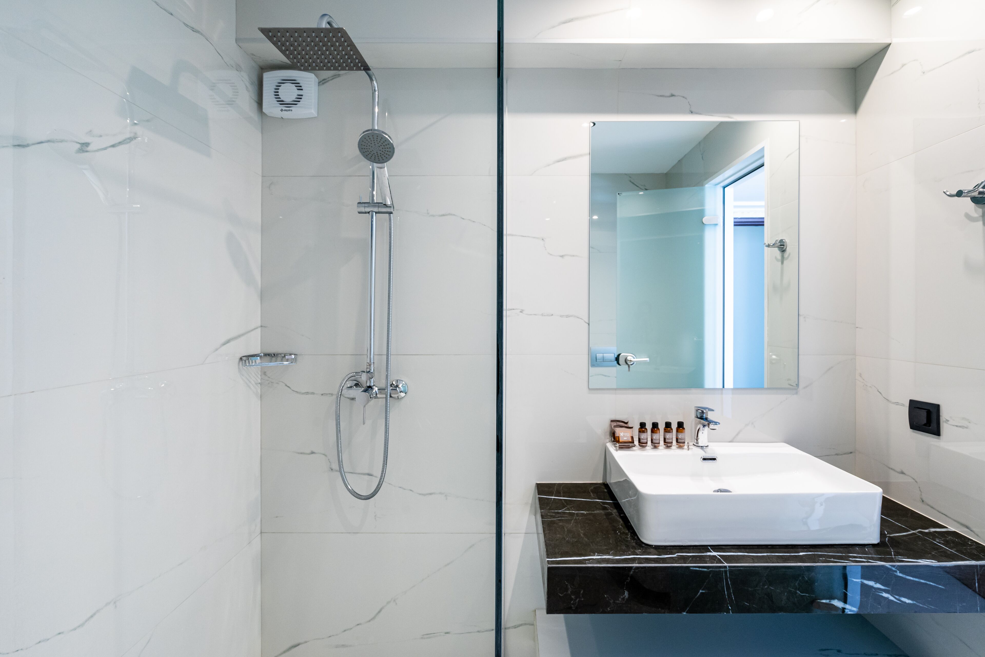 Ein modernes Badezimmer mit einer Duschkabine aus Glas, einem weißen Waschbecken mit schwarzer Marmorplatte und einem großen Spiegel darüber.
