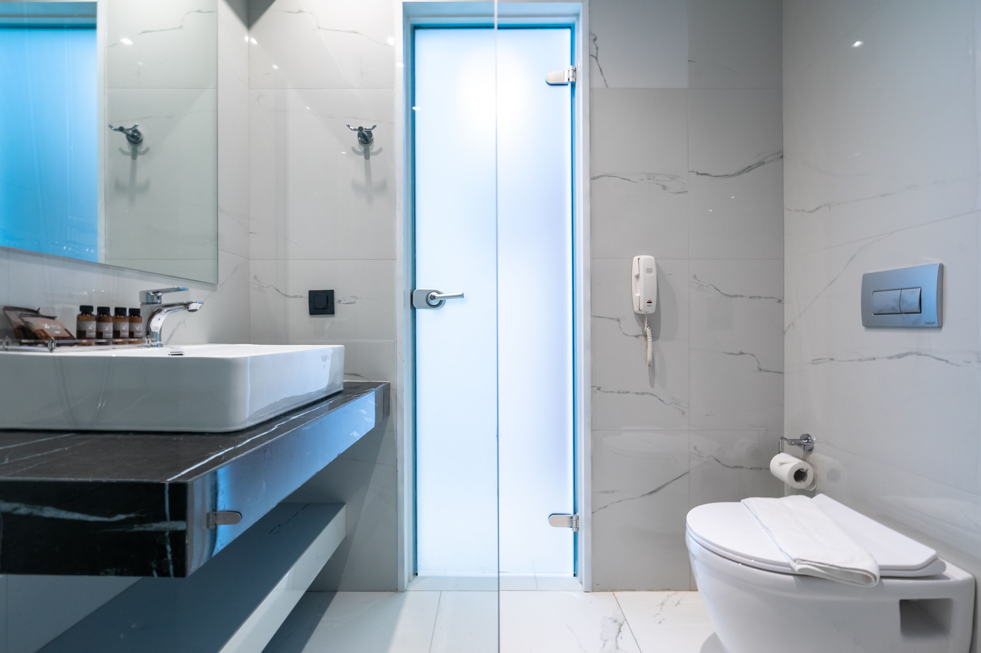 Un baño moderno con mampara de vidrio, lavamanos blanco y retrete.