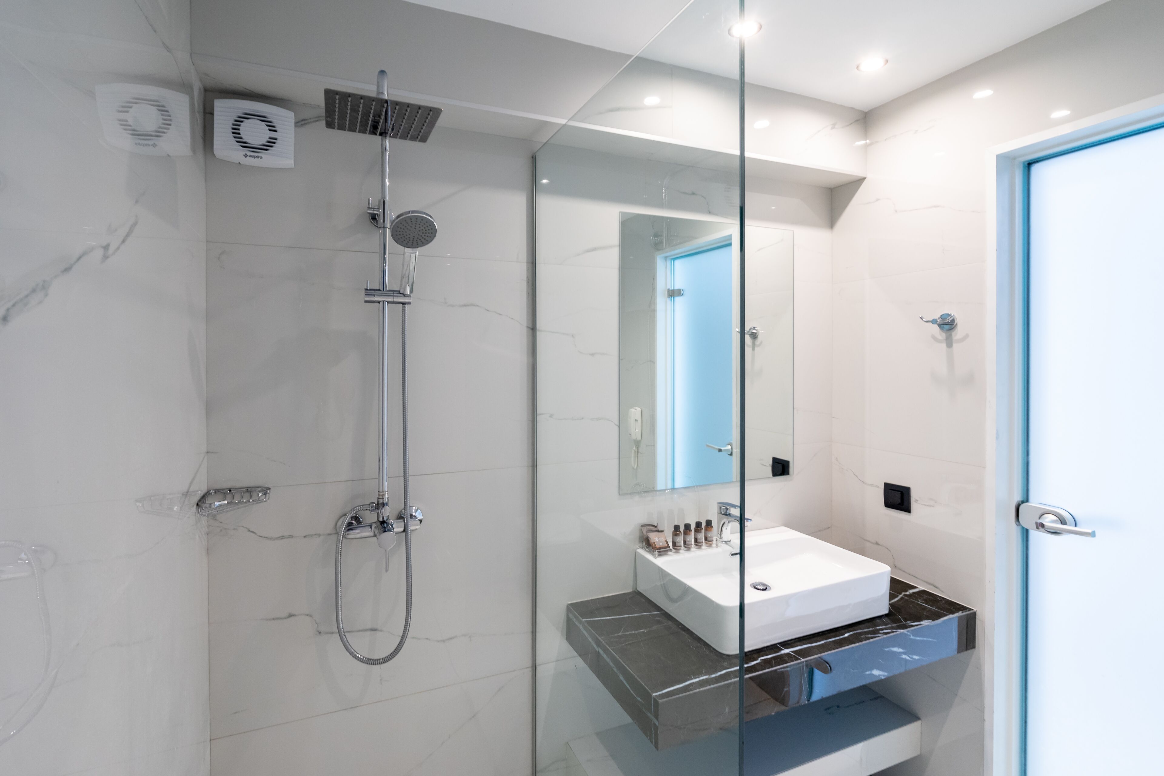 Un baño moderno con ducha envuelta en vidrio, un lavabo blanco sobre encimera de mármol y un espejo grande.