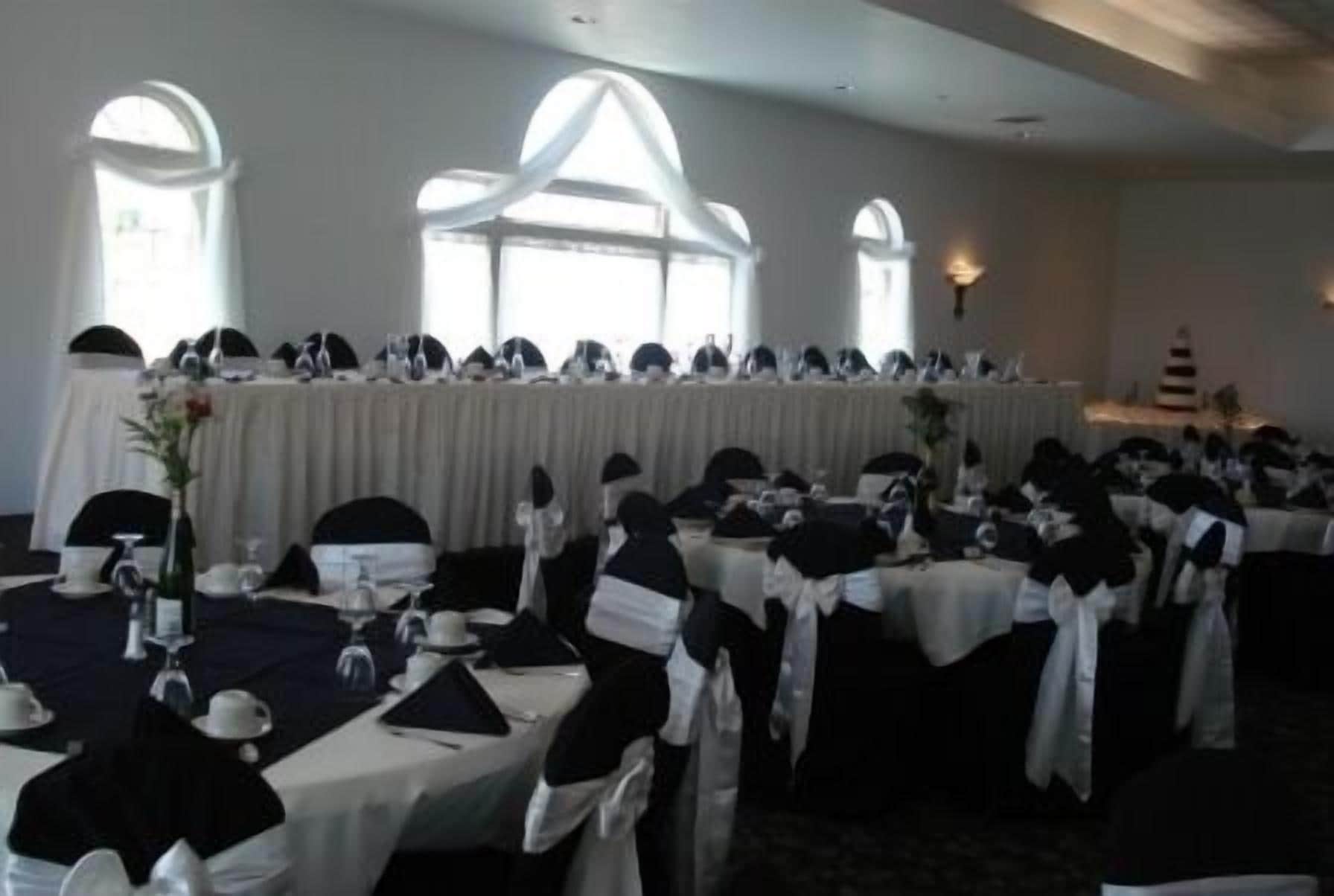 A banquet hall with round tables set for a formal event, featuring white tablecloths and black chair covers.