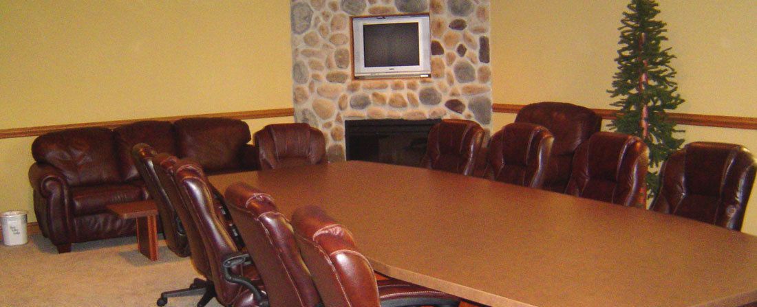 A conference room with a long table and leather chairs, a stone fireplace, and a television mounted on the wall.