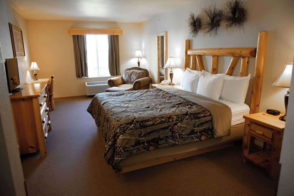 A bedroom with a bed, a wooden headboard, a desk, a chair, a window, and a wall-mounted air conditioner.