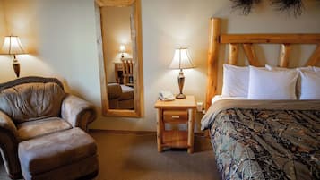 Ein Schlafzimmer mit einem Holzkopfteil, einem Bett mit weißen Leinen, einem Ledersessel, einem Nachttisch aus Holz mit einer Lampe und einem Spiegel an der Wand.