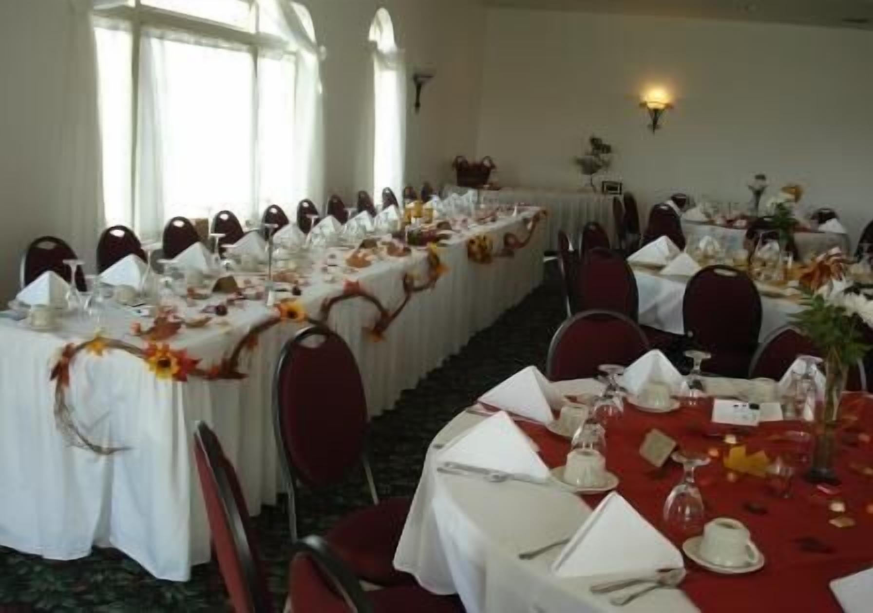 Une salle de banquet où de longues rangées de tables sont dressées pour un événement formel, chacune étant recouverte d’une nappe blanche et agrémentée de chaises rouges.