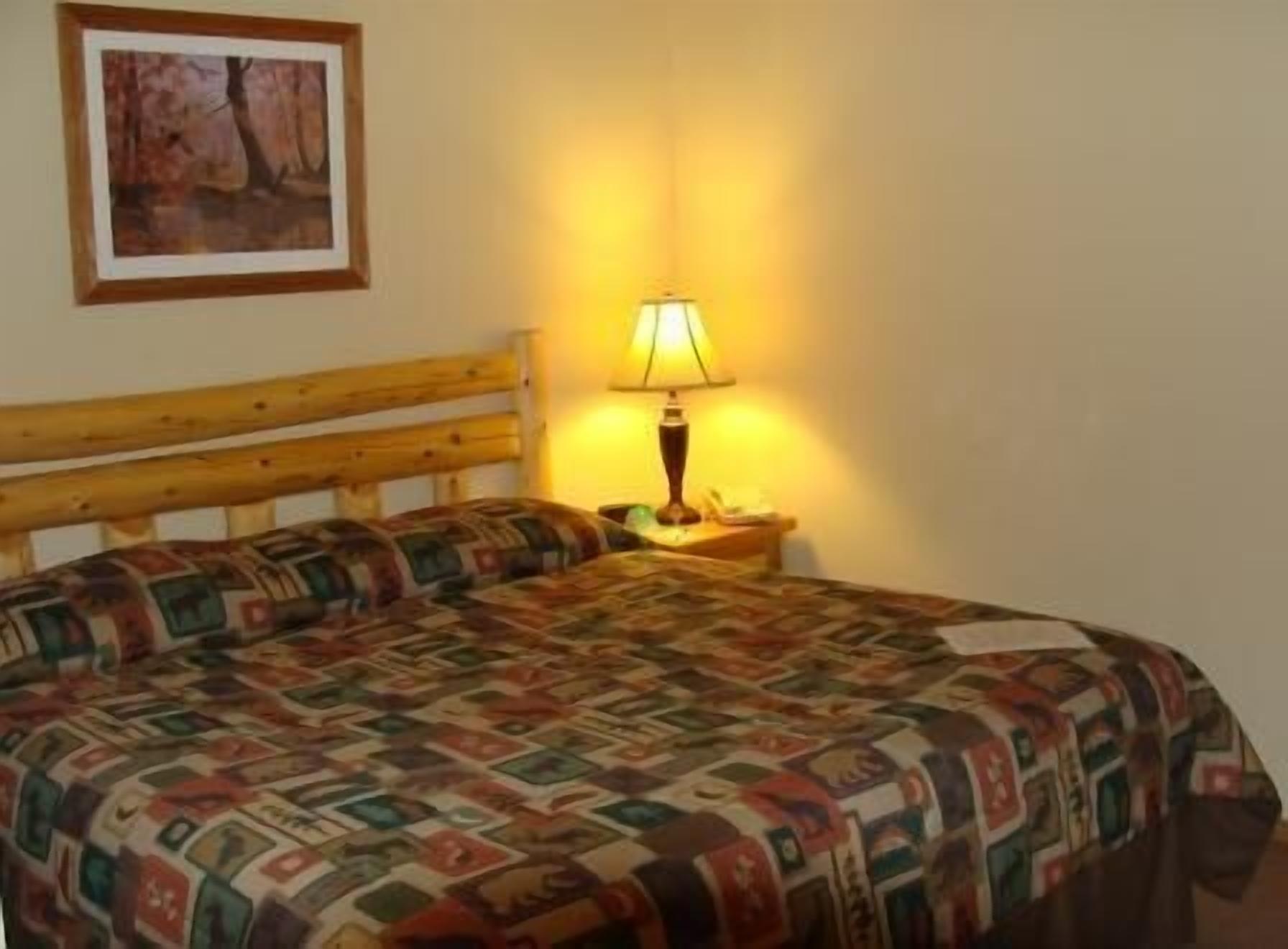 Una habitación con cabecera de madera, colcha estampada, lámpara de noche y un cuadro en la pared.