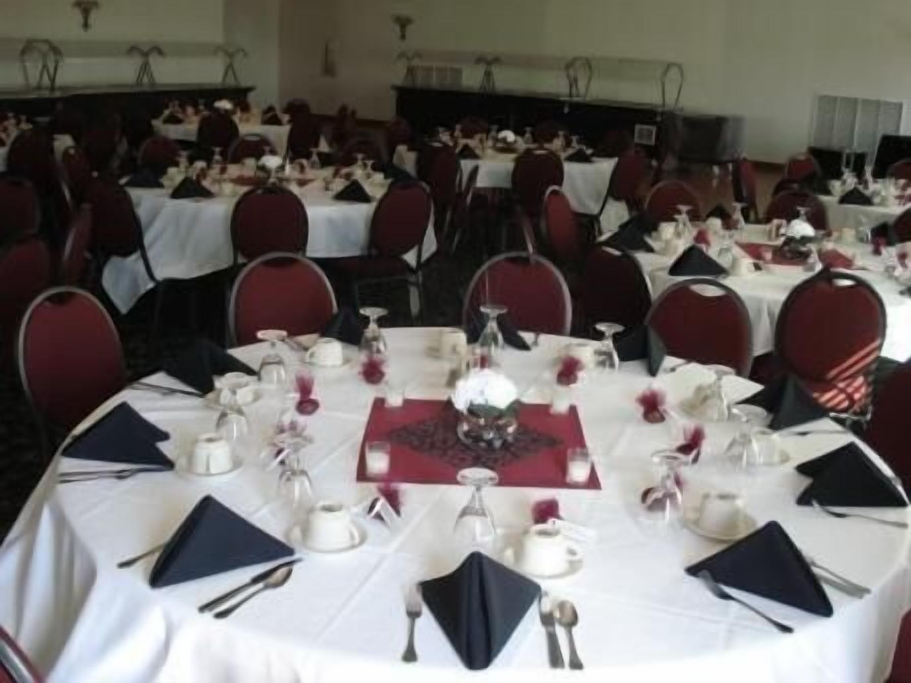 A banquet hall with round tables set for a formal event, each with white tablecloths, red chairs, and neatly arranged tableware.