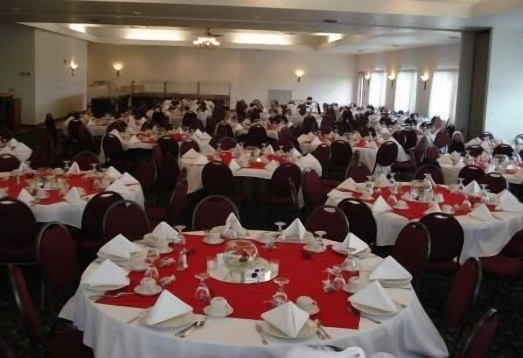 A banquet hall with round tables covered in white tablecloths and red table runners, arranged in rows.
