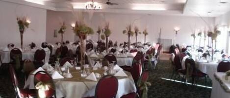 Un salón de banquetes con mesas redondas dispuestas para un evento formal, con manteles blancos y sillas rojas.