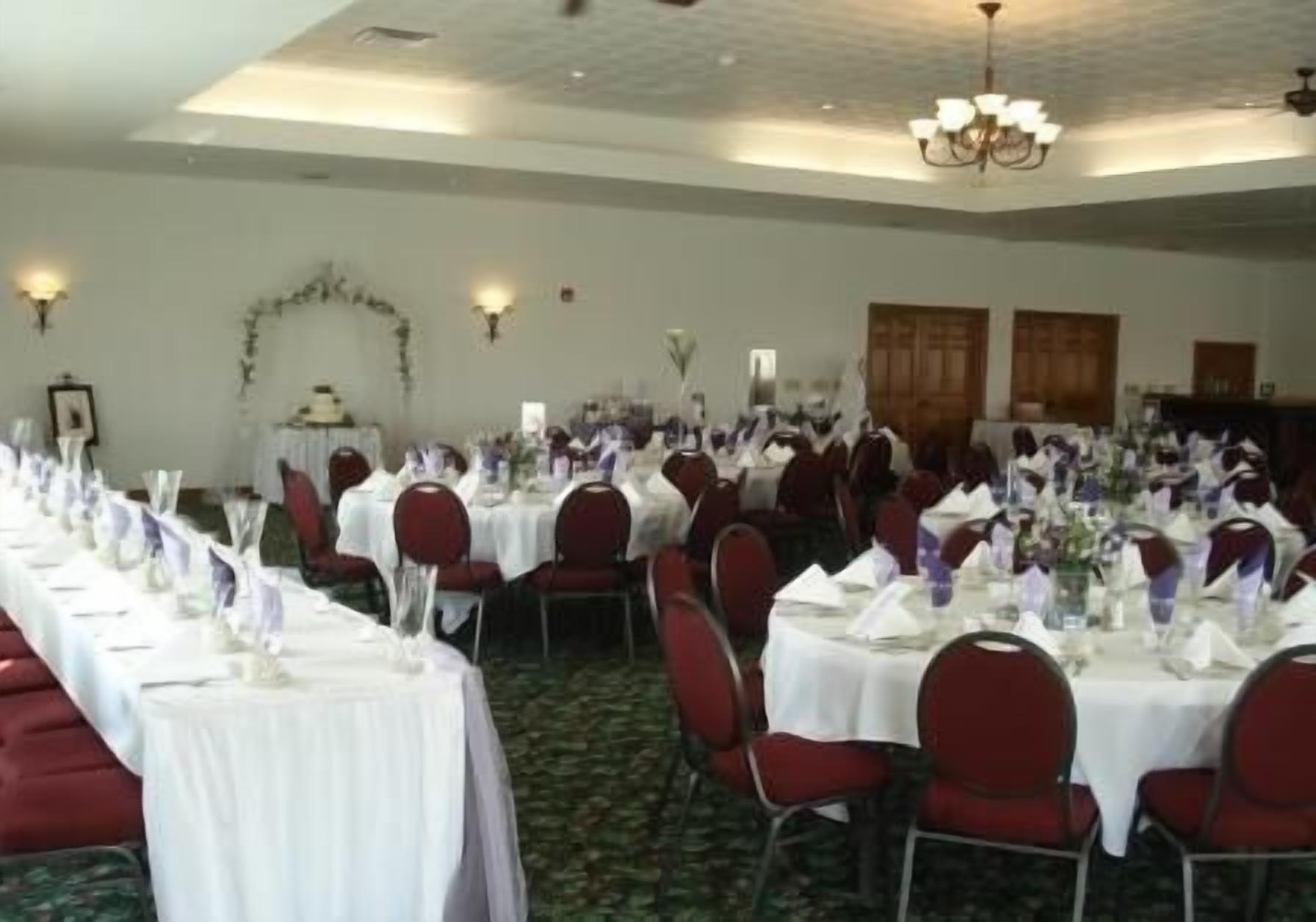 A banquet hall with rows of round tables, each set with white tablecloths and red chairs.