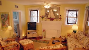 A cozy living room with wicker furniture, a fireplace, and a television. - Sun N Fun Beachfront Vacation Rentals (Indian Shores)