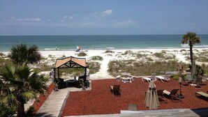 A beachside patio with lounge chairs, a covered seating area, and a view of the ocean. - Sun N Fun Beachfront Vacation Rentals (Indian Shores)