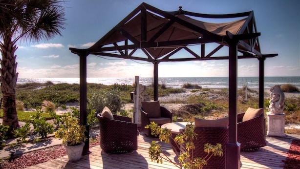 A wooden deck with wicker furniture and a pergola overlooking a beach. - Sun N Fun Beachfront Vacation Rentals (Indian Shores)
