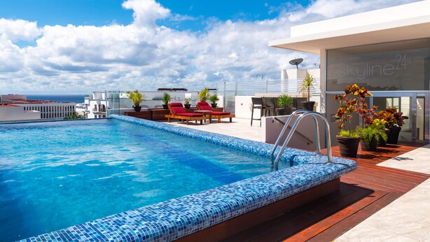A rooftop pool with a blue mosaic edge, red lounge chairs, and potted plants.
