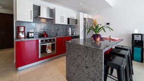 A modern kitchen with granite countertops, red and white cabinetry, a built-in oven, a microwave, and a coffee maker.